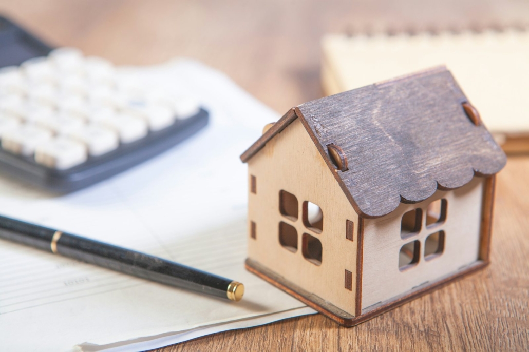 Immobilienbewertung Aschheim: Hausmodell aus Holz mit Taschenrechner und Stift