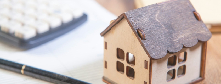 Immobilienbewertung Aschheim: Hausmodell aus Holz mit Taschenrechner und Stift