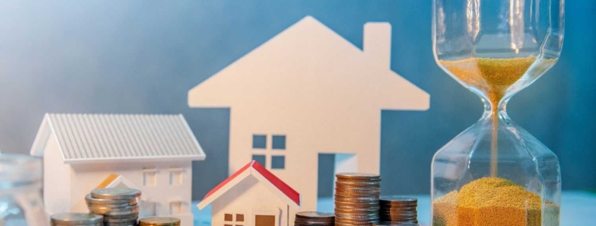 Immobilienbewertung Forstern: Hausmodell mit Sanduhr und Münzen als Symbol für Wert und Zeitpunkt